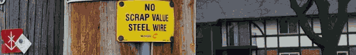 a metal sign reading "no scrap value steel wire" pinned and nailed over wire going up a telephone pole